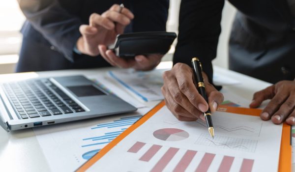 A group of Asian businessmen are brainstorming to analyze financial reporting situations. Calculate investments with income, tax and accounting calculators from graphs data on laptop at desk.