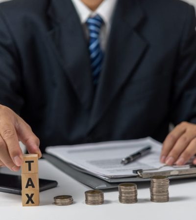 Businessman holding Wood Cube Tax Coin Financial Concept Design with a stack of coins. Business finance, accounting.