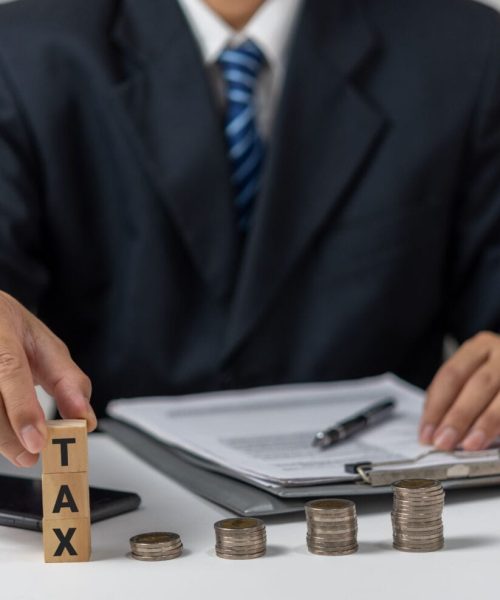 Businessman holding Wood Cube Tax Coin Financial Concept Design with a stack of coins. Business finance, accounting.