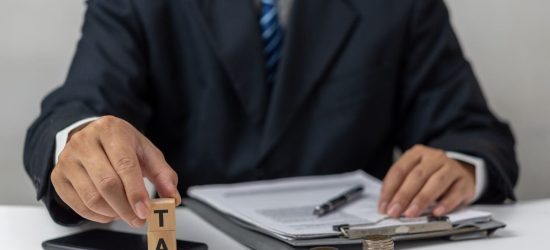 Businessman holding Wood Cube Tax Coin Financial Concept Design with a stack of coins. Business finance, accounting.