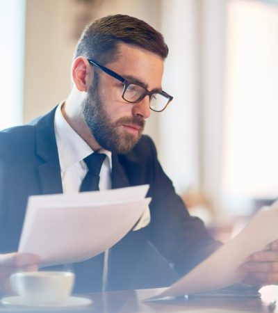 Confident banker reading financial papers while sitting in cafe