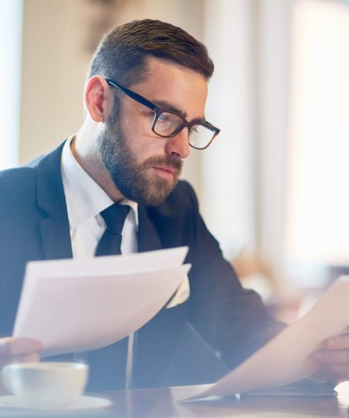 Confident banker reading financial papers while sitting in cafe