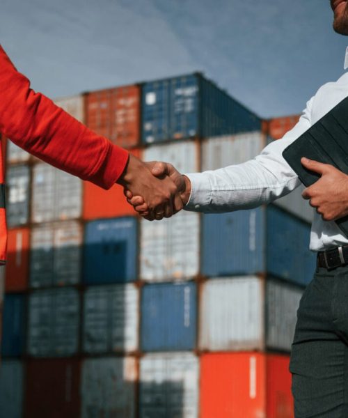 Making handshake. Two male workers is on the location with containers.