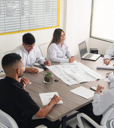 Person with vitiligo in a work environment. Business meeting and project planning at an engineering company. A business meeting at an engineering firm, where professionals discuss projects and delivery dates. Participants review blueprints, take notes, and analyze a whiteboard to make strategic decisions. The atmosphere is collaborative and focused on achieving set goals.