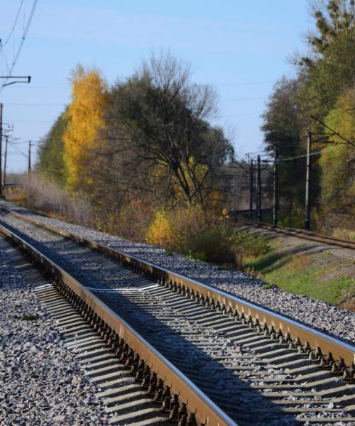 Autumn industrial landscape. Railway receding into the distance among green and yellow autumn trees