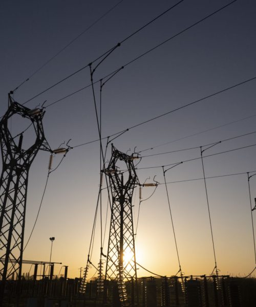 Photographic documentation of the silhouettes of high voltage pylons against a twilight sky with warm and cold tones.