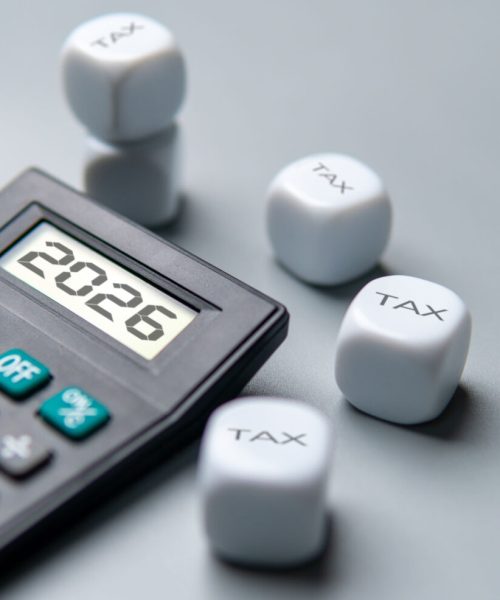 A calculator displaying the year 2026 surrounded by dice labeled TAX. Financial planning, taxation, accounting, and budget concepts.